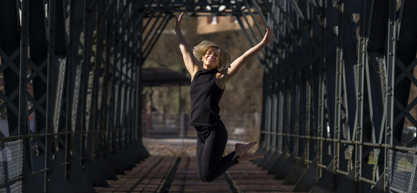 Antje Krämer auf einer Stahlbrücke, freudig in der Luft — Achtsame Körperarbeit