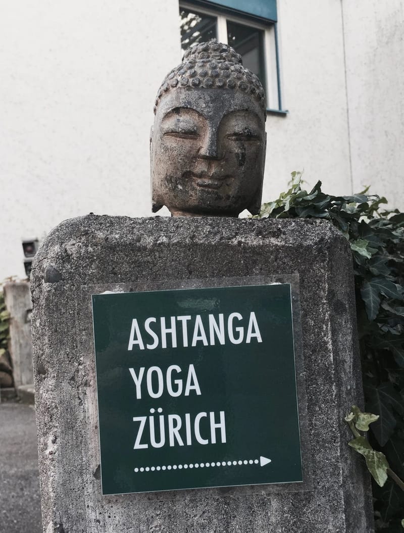 Buddha-Kopf mit dem grünen Schild von Ashtanga Yoga Zürich am Eingang der Shala