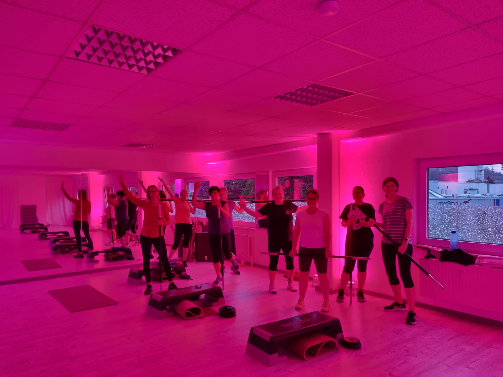 Hot-Iron-Kurs mit Langhanteln im magentafarben beleuchteten Kursraum von BeFit Alfeld