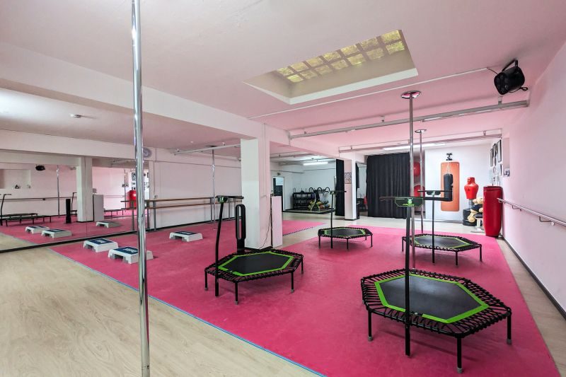 Kursraum von Body & ART mit pinkem Boden, Poledance-Stangen, Jumping-Trampolinen und Boxsack