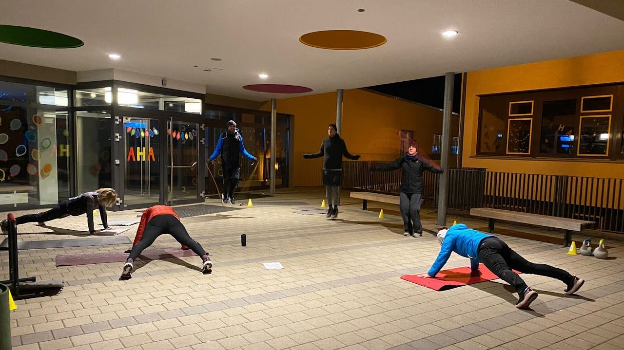 Outdoor-Circuit von burpee & run am Abend unter einem überdachten Bereich, Teilnehmer bei Planks und Seilspringen
