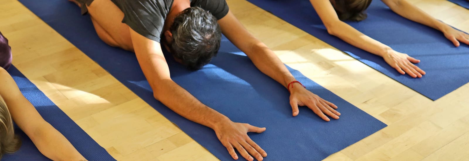 Gruppe in einer Yoga-Vorbeuge auf blauen Matten im Studio