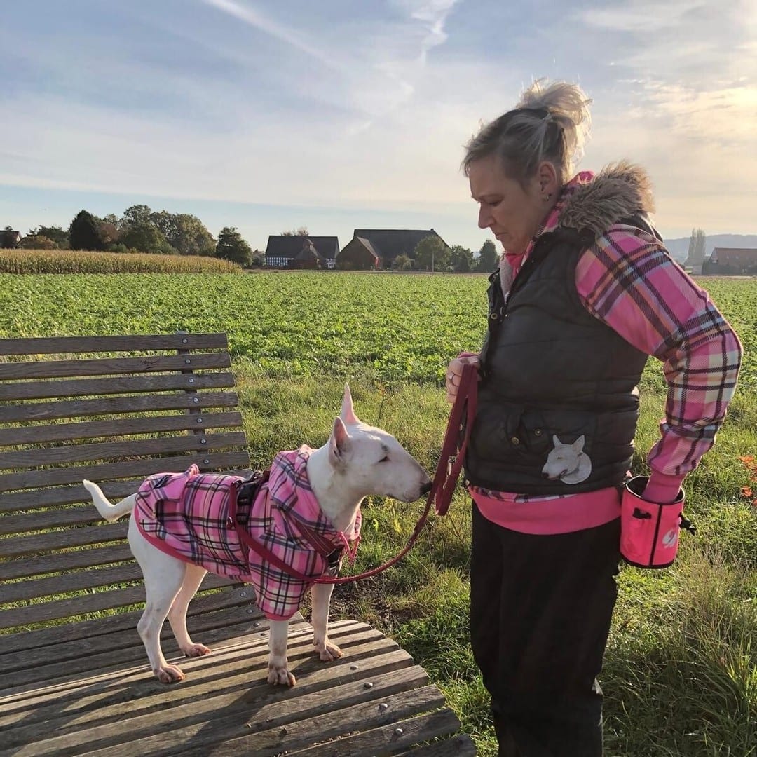 Jennifer Schürmann mit ihrem weißen Bullterrier im pinken Mantel auf einem Feldweg bei Bad Essen
