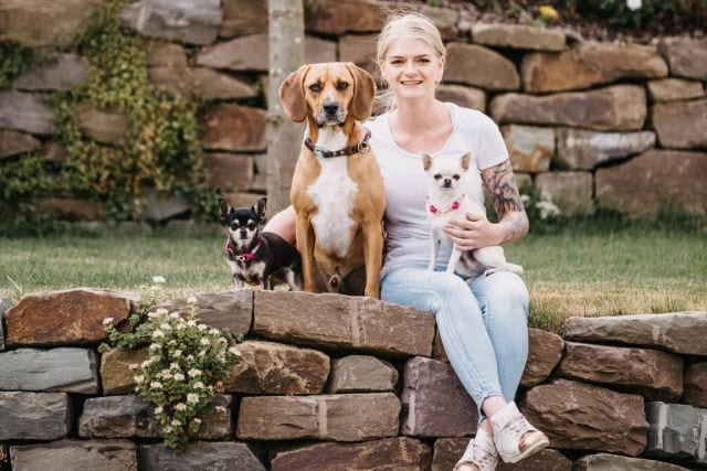 Marleen Schaks sitzt mit ihren beiden Chihuahuas und ihrem Mischlingsrüden auf einer Natursteinmauer