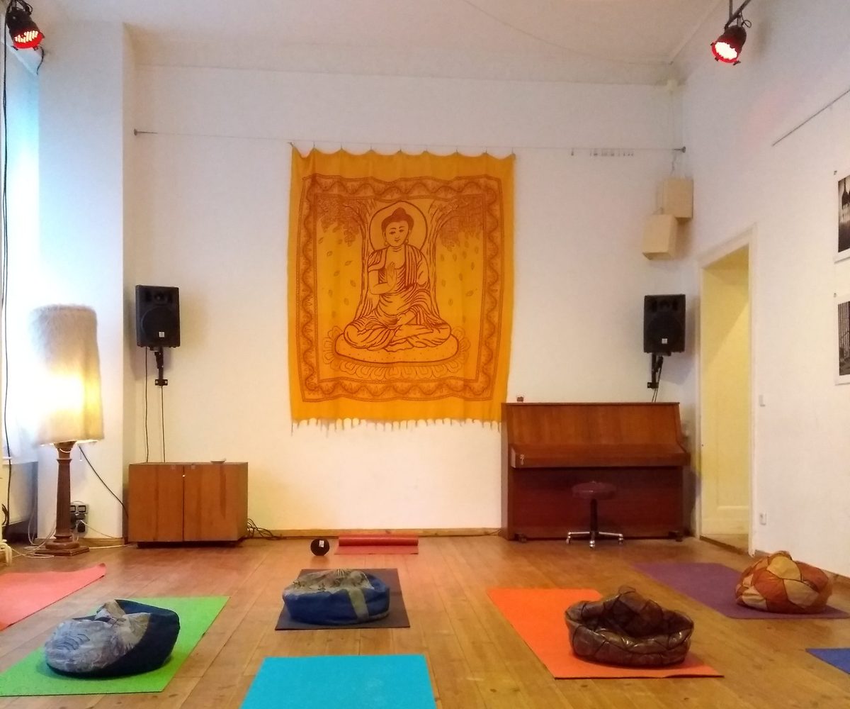 Heller Bewegungsraum im Kulturcafé Fincan mit Buddha-Wandbehang, bunten Yogamatten und Klavier