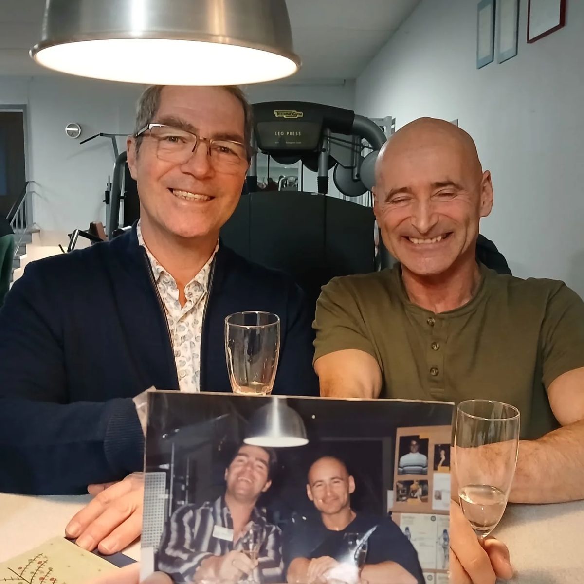 Johannes und Andreas sitzen mit Sektgläsern im Studio und halten ihr gemeinsames Foto von Januar 2004 in die Kamera