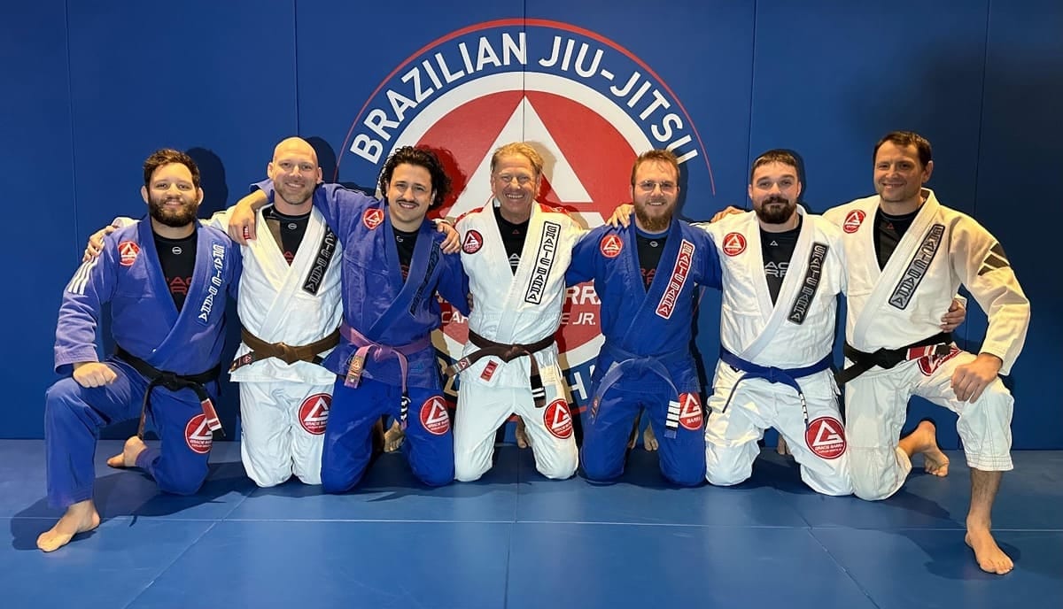 Sieben Trainer von Gracie Barra Alsterdorf knien vor der blauen Mattenwand mit dem Brazilian-Jiu-Jitsu-Logo