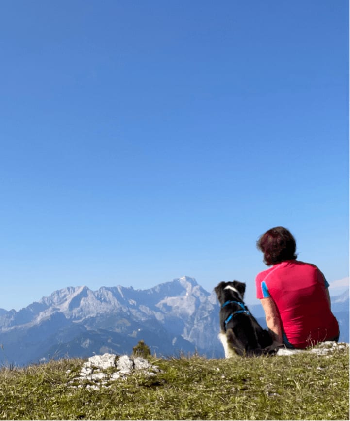 Andrea sitzt mit Neela auf einer Bergwiese und schaut auf die Gipfel des Wettersteingebirges