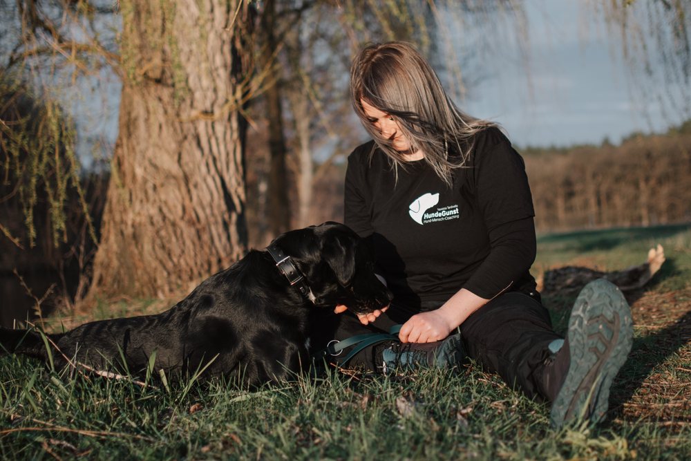 Katha, Hundetrainerin bei HundeGunst, kniet im Abendlicht neben einem Hund