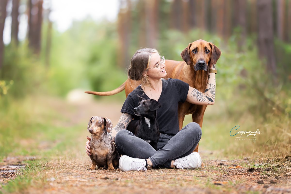 Vanessa Tardivello sitzt auf einem Waldweg zwischen ihren drei Hunden