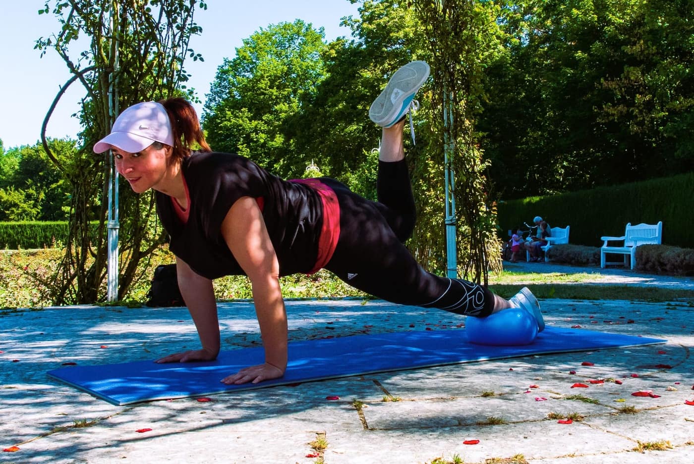 Julia beim Training auf der Matte im Grünen, gestützter Plank mit angehobenem Bein