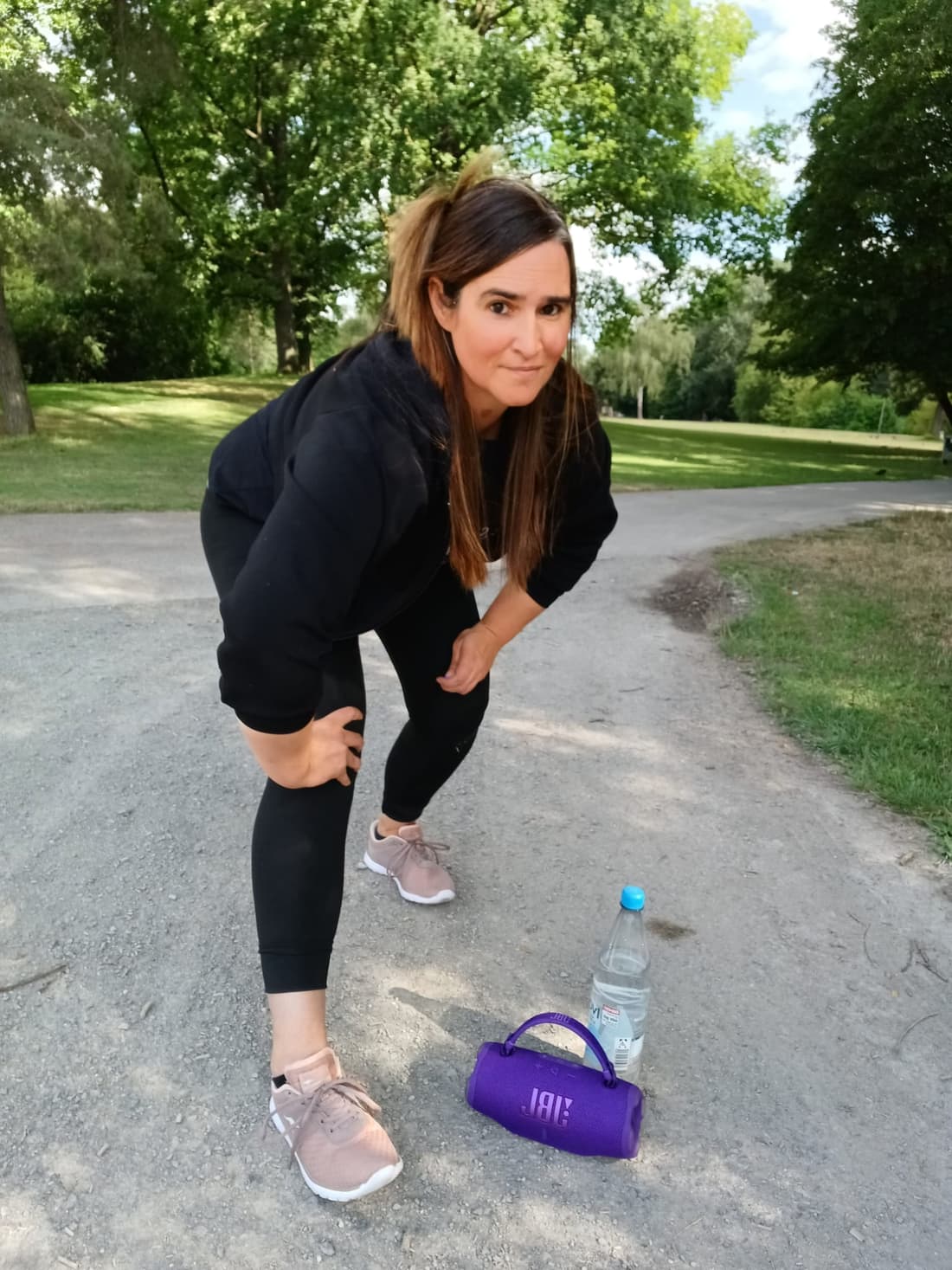 Julia auf einem Parkweg im Grünen, daneben eine Wasserflasche und eine Musikbox