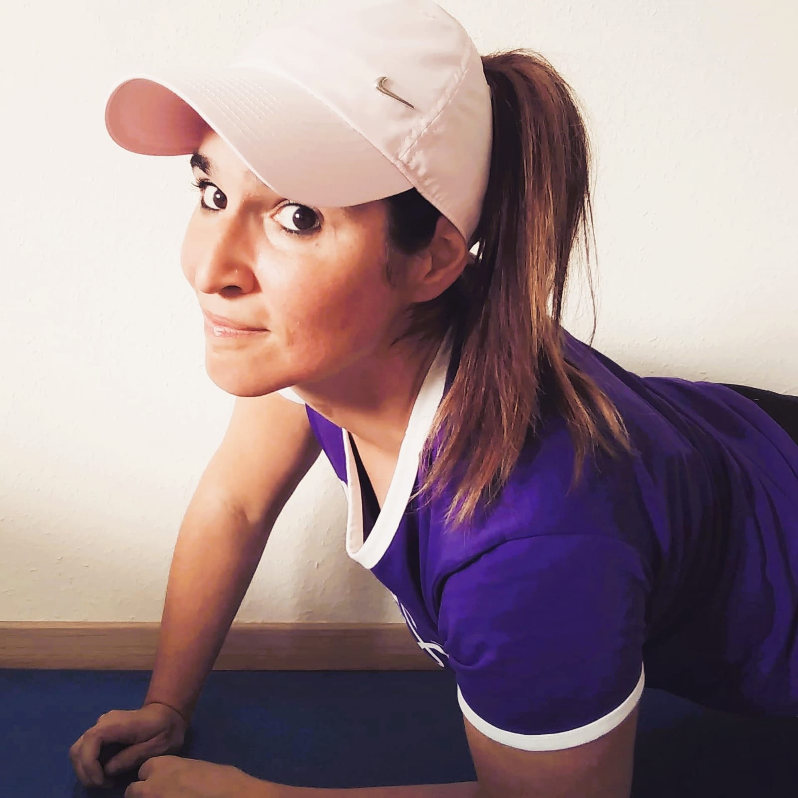 Julia mit rosa Cap und lila Sportshirt, aufgestützt auf der blauen Trainingsmatte