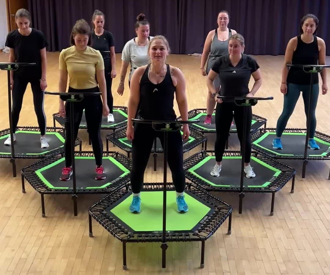 Gruppe auf grünen Jumping-Trampolinen im Montfortsaal, vorne die Trainerin
