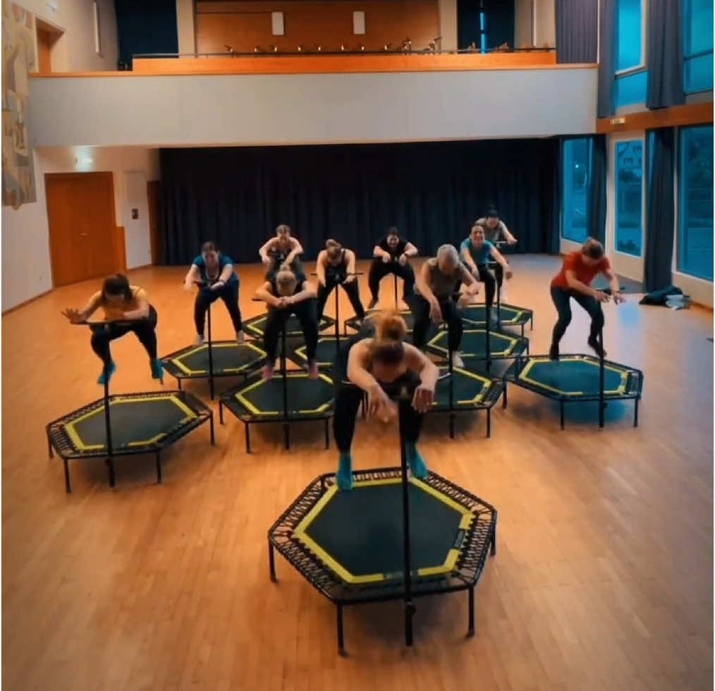 Jumping-Fitness-Stunde im Montfortsaal Weiler: zwölf Frauen in der Hocke auf Trampolinen mit Haltestange