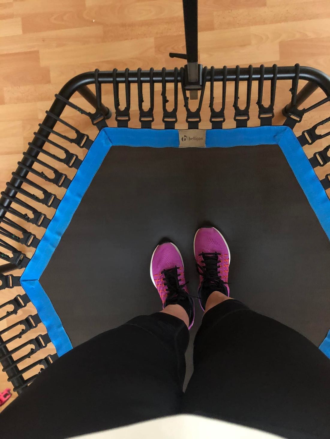 Blick von oben auf ein bellicon-Trampolin mit blauem Rand, pinke Sportschuhe stehen auf der Sprungfläche