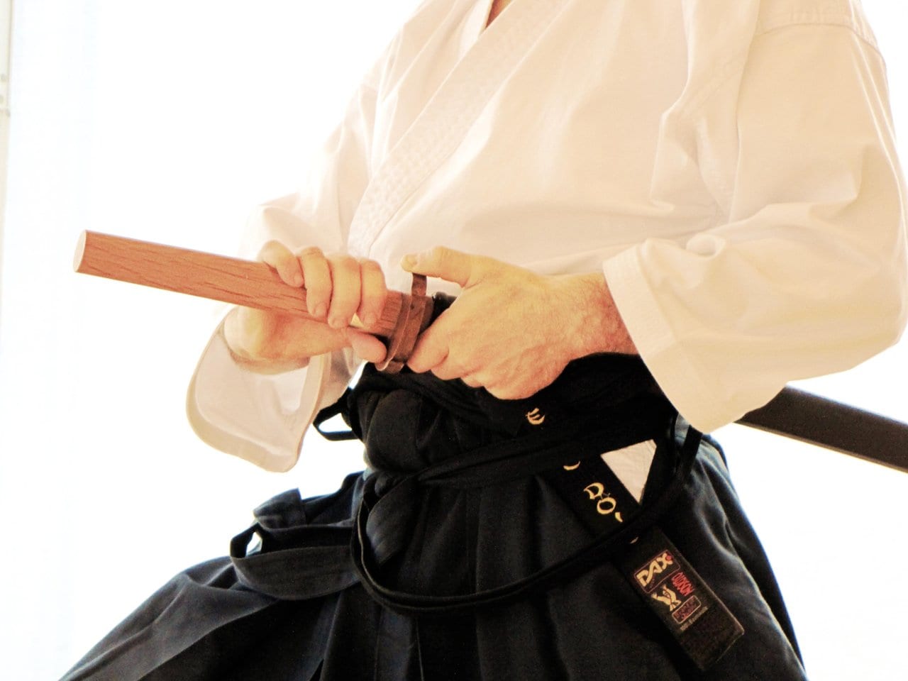 Trainingsdetail aus dem Keiko Dojo: Hände am Jo-Stab, schwarzer Gürtel und Hakama