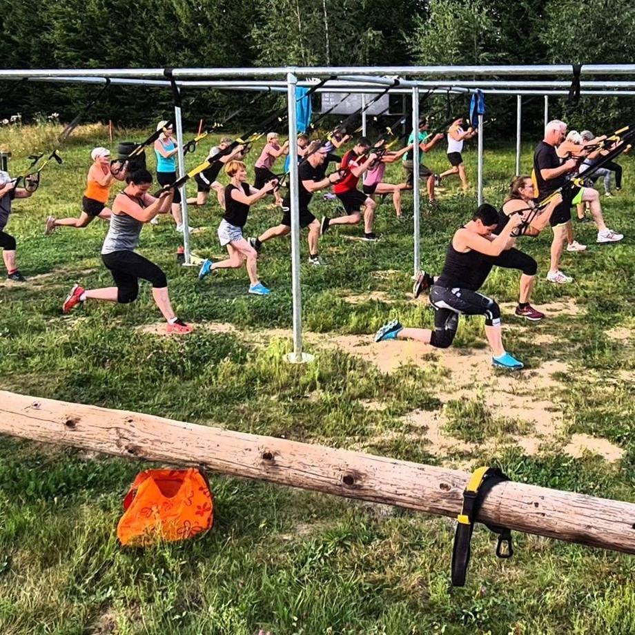 TRX-Kurs an der Outdoor-Anlage von Kraftwerker Sport, viele Trainierende an Schlingentrainern auf der Wiese