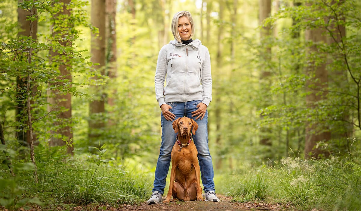 Lisa Eitel steht mit ihrem Vizsla Tabo auf einem Waldweg
