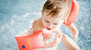 Kind mit Schwimmflügeln beim Babyschwimmen im warmen Wasser