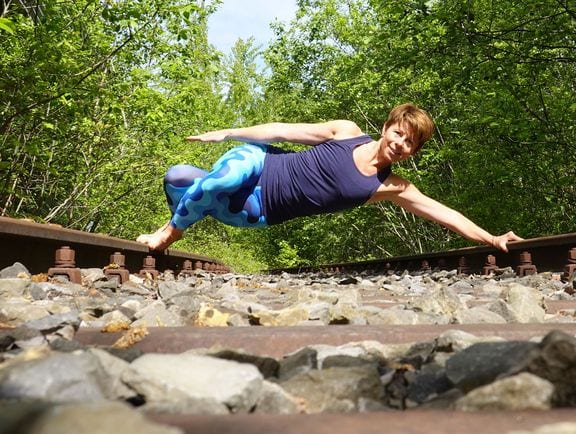 Silvia Meier in einer Pilates-Plank-Pose auf Eisenbahngleisen im Wald