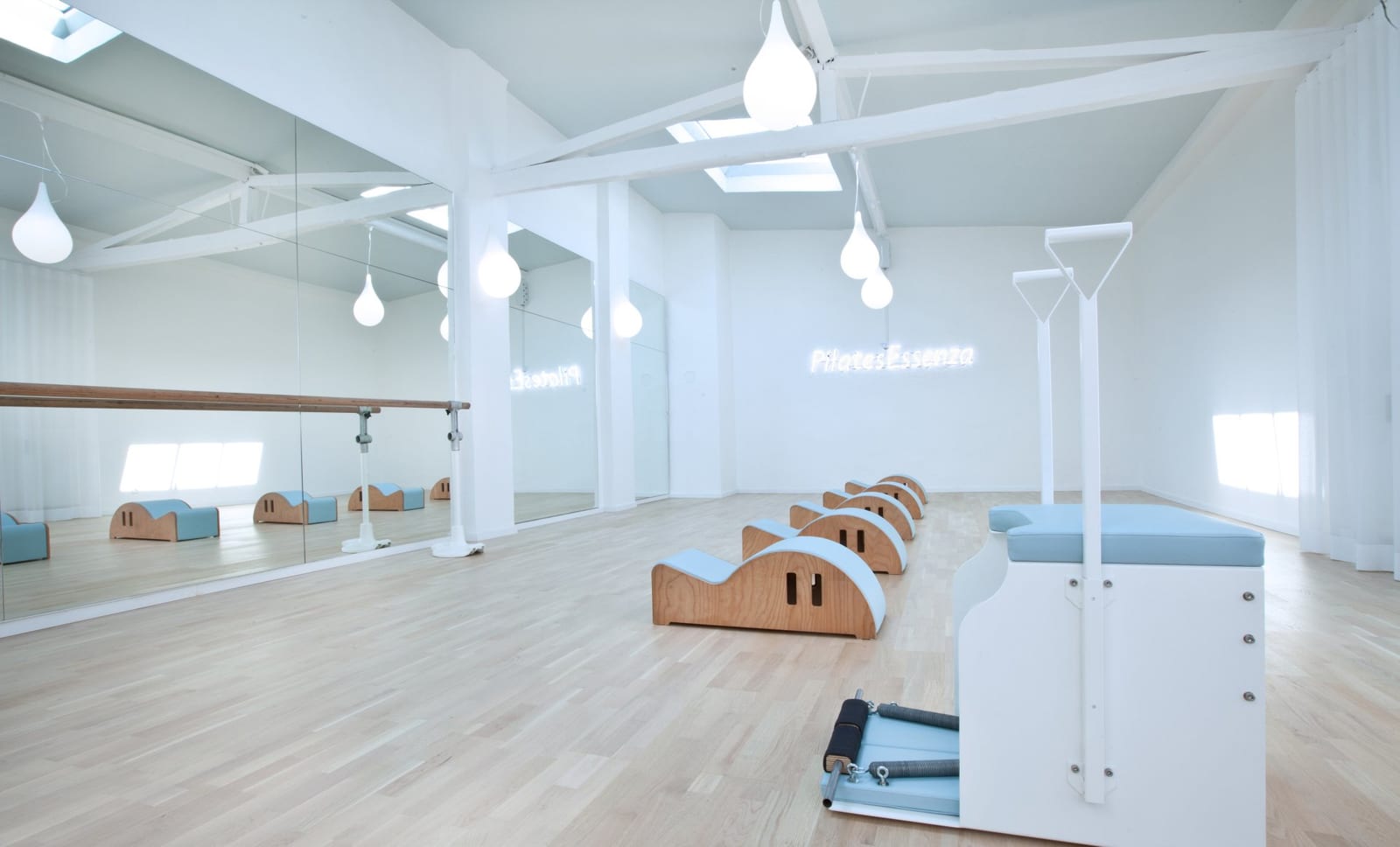 Heller Pilates-Studioraum von Pilates Essenza mit Geräten, Spiegelwand und Neon-Schriftzug