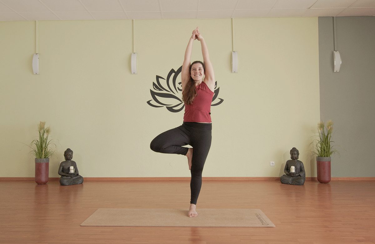 Yogalehrerin in der Baumhaltung vor dem Lotus-Wandbild im Pura Vida Yoga Center Kempten