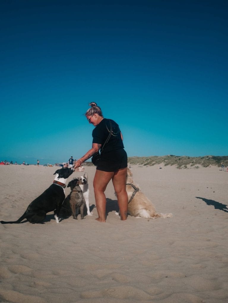 Maureen Smith steht am Strand, vier Hunde sitzen ruhig um sie herum