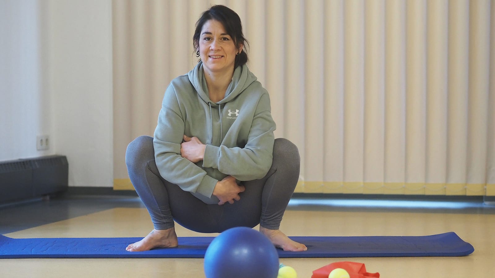 Johanna Roth sitzt auf einem Gymnastikball im Kursraum und lächelt in die Kamera