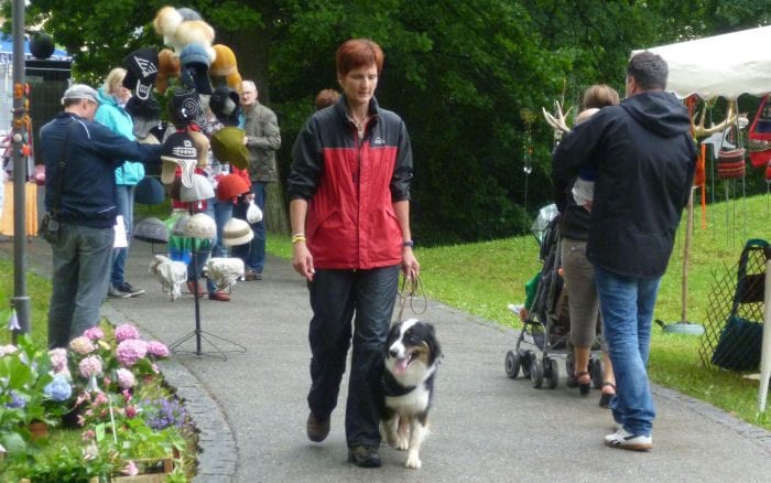 Claudia Pöschl geht mit einem Australian Shepherd entspannt durch eine belebte Gasse