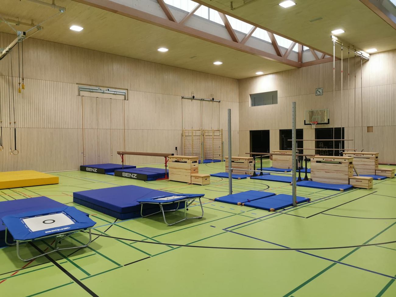 Aufgebaute Gerätelandschaft in der Halle: Trampoline, Sprungkästen, Barren und blaue Matten
