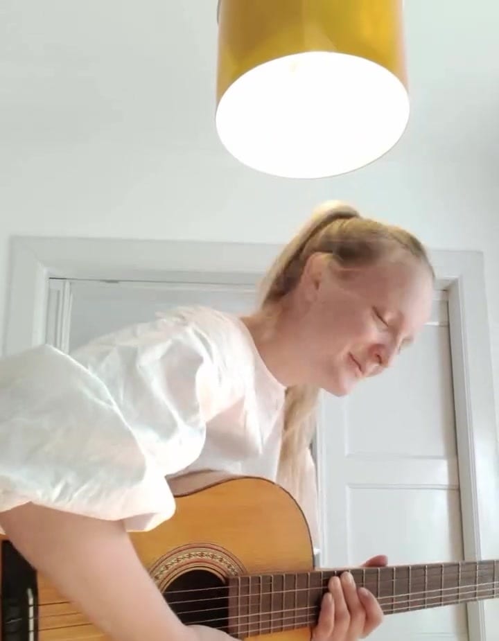 Lilian singt mit geschlossenen Augen zur Gitarre, über ihr eine gelbe Lampe
