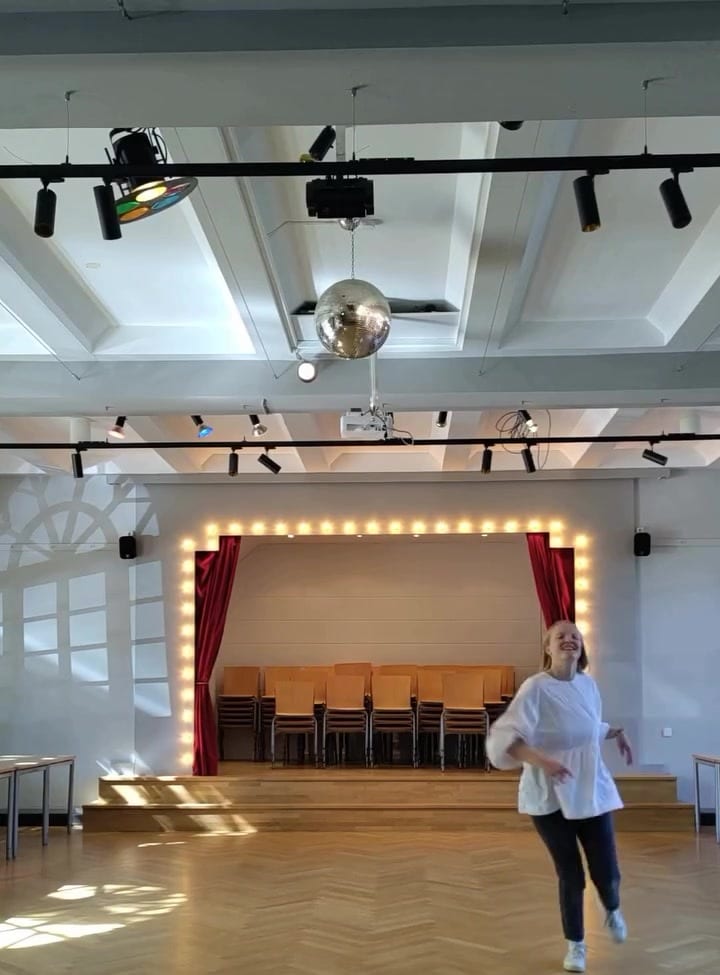 Lilian tanzt lachend durch den leeren Steenkampsaal, im Hintergrund die beleuchtete Bühne